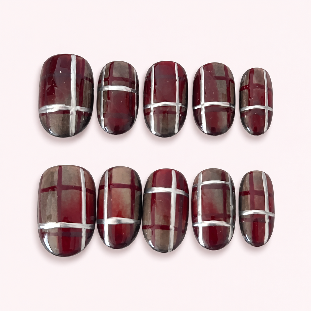 St. Agnes burgundy plaid cateye press-on nails on a pale pink background