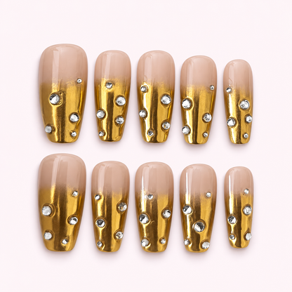 Mansa Musa gold chrome rhinestone press-on nails on a pale pink background
